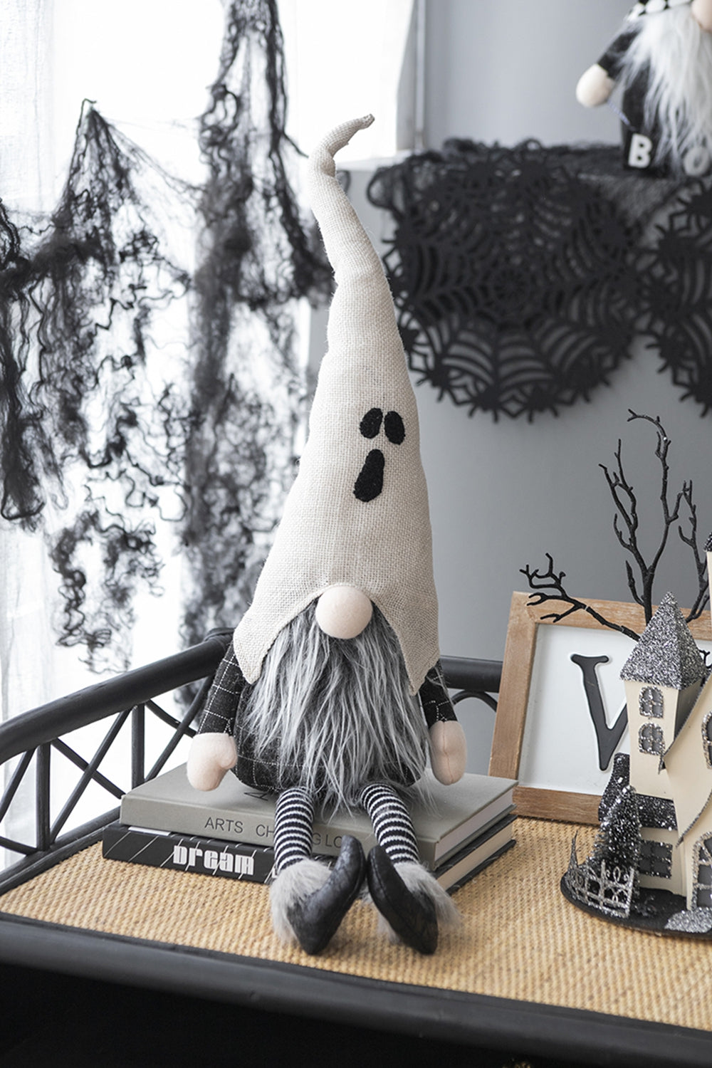 Seated Halloween gnome with a white ghost-face hat, gray beard, striped legs and black shoes in a tabletop display.