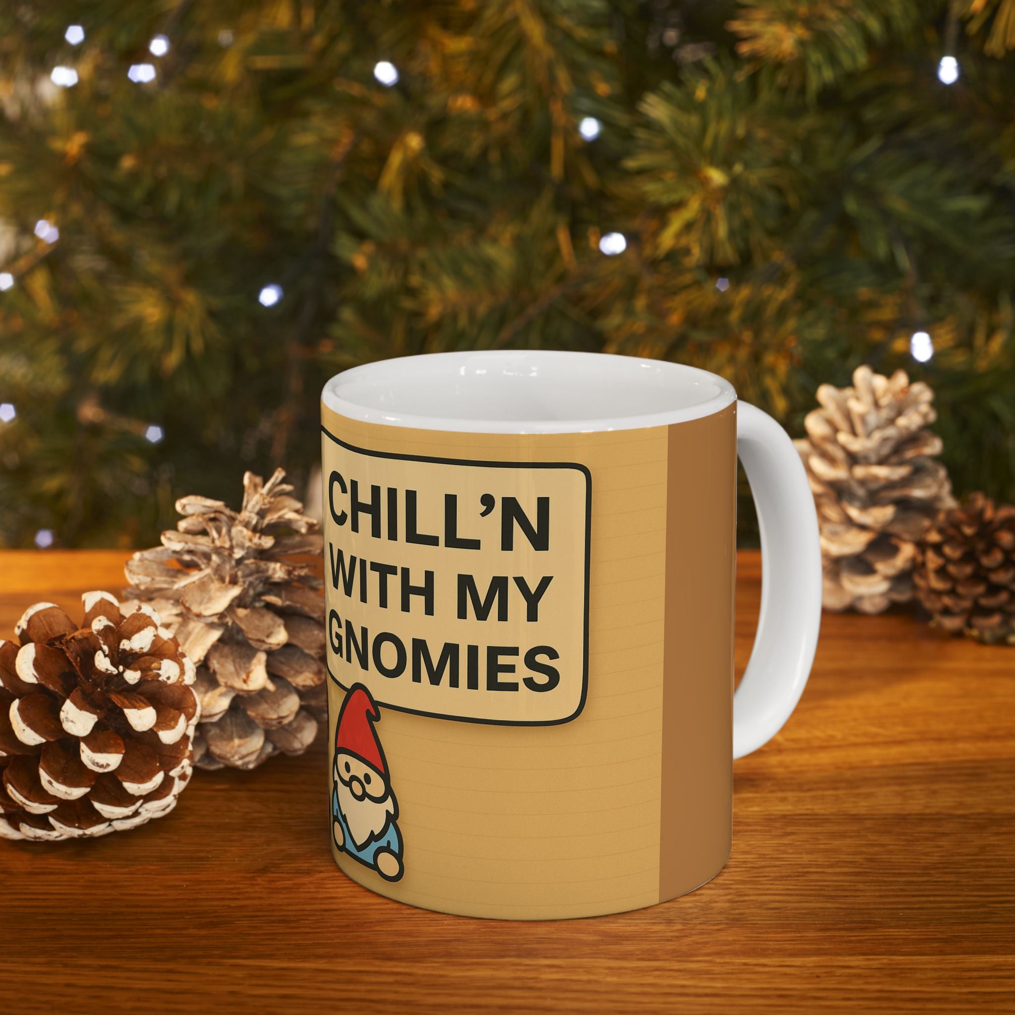 Beige mug with 'Chill'n with my Gnomies' text and gnome illustration on a wooden surface with pinecones and a Christmas tree in the background.