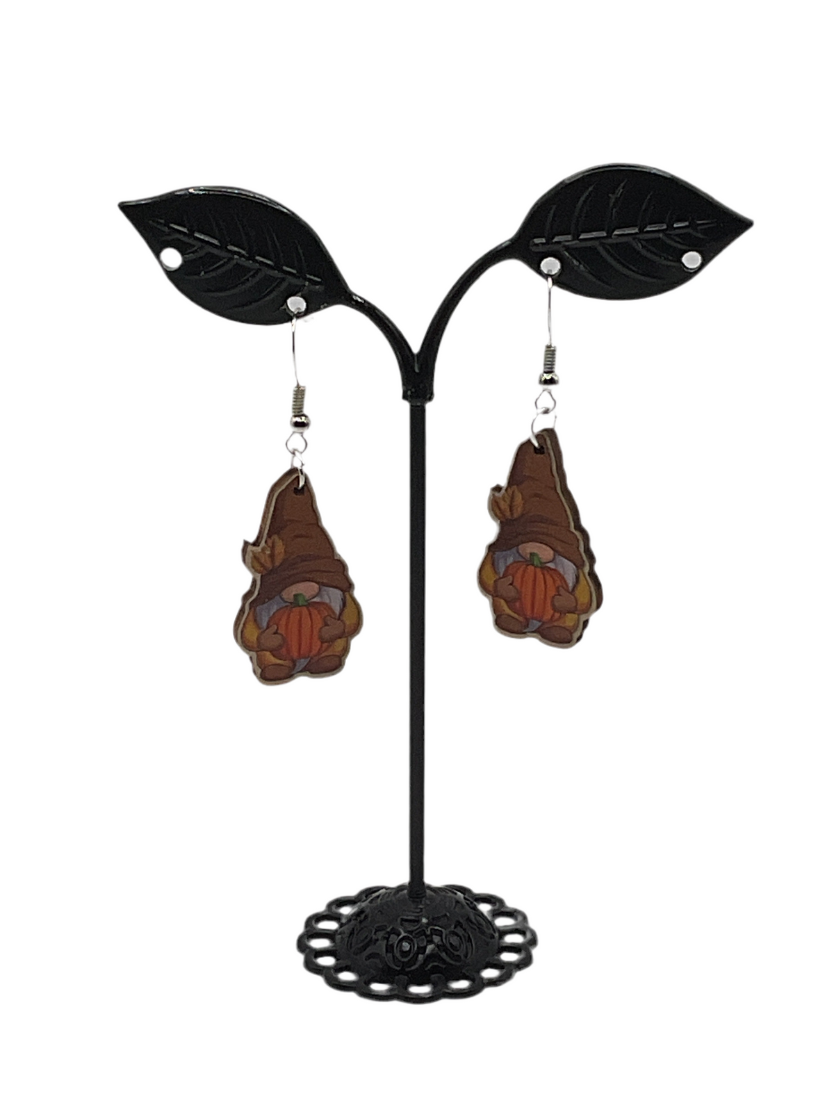 Pair of brown-hatted gnome earrings holding orange pumpkins, hanging from a black leaf-shaped jewelry stand.