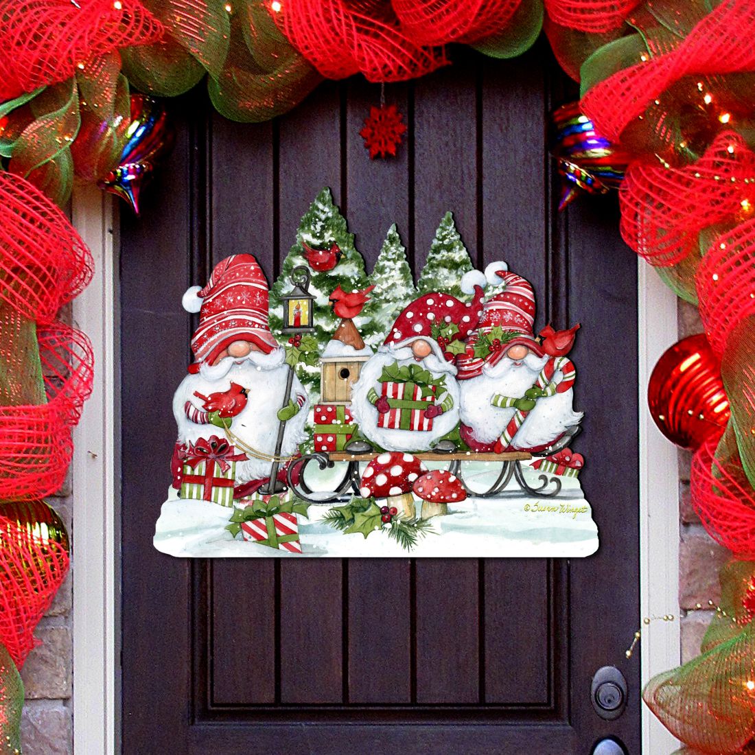 Door decoration showing three red-hatted Christmas gnomes with gifts, candy canes, cardinals and snowy trees.