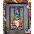 Halloween door decoration with a blue-hatted gnome holding a jack-o'-lantern; its hat depicts a witch, moon and haunted house.