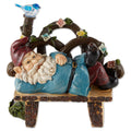 Gnome resting on a wooden-style bench with flowers and a blue bird, wearing a teal coat and red hat.