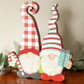 Two wooden tabletop gnomes with white fluffy beards, checked and striped hats, a candy cane and a teal gift.