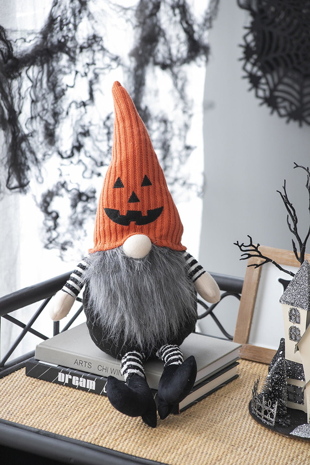 Seated Halloween gnome with an orange jack-o'-lantern hat, gray beard and black-and-white striped arms and legs.