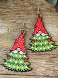 Pair of drop earrings shaped like Christmas tree gnomes with red spotted hats, white mustaches and green branches.
