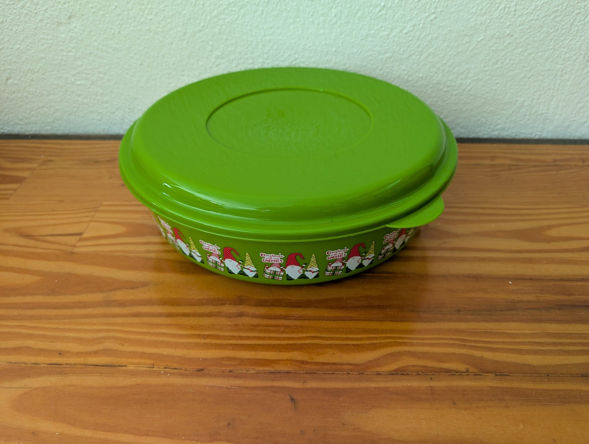 Lime green lidded bowl with a Christmas gnome pattern around its sides, displayed on a wooden tabletop.