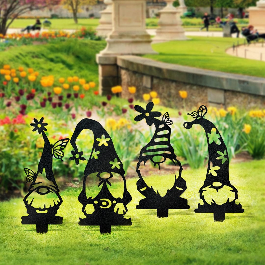 Four black metal gnome garden stakes with flower and butterfly hat details displayed on a lawn.