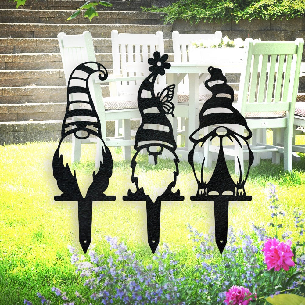Three black metal gnome garden stakes with striped hats, flower and butterfly details, displayed on a lawn.