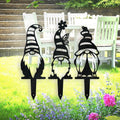 Three black metal gnome garden stakes with striped hats, flower and butterfly details, displayed on a lawn.