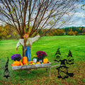 Four black Halloween gnome yard stakes arranged beside a scarecrow, pumpkins and an autumn garden cart.