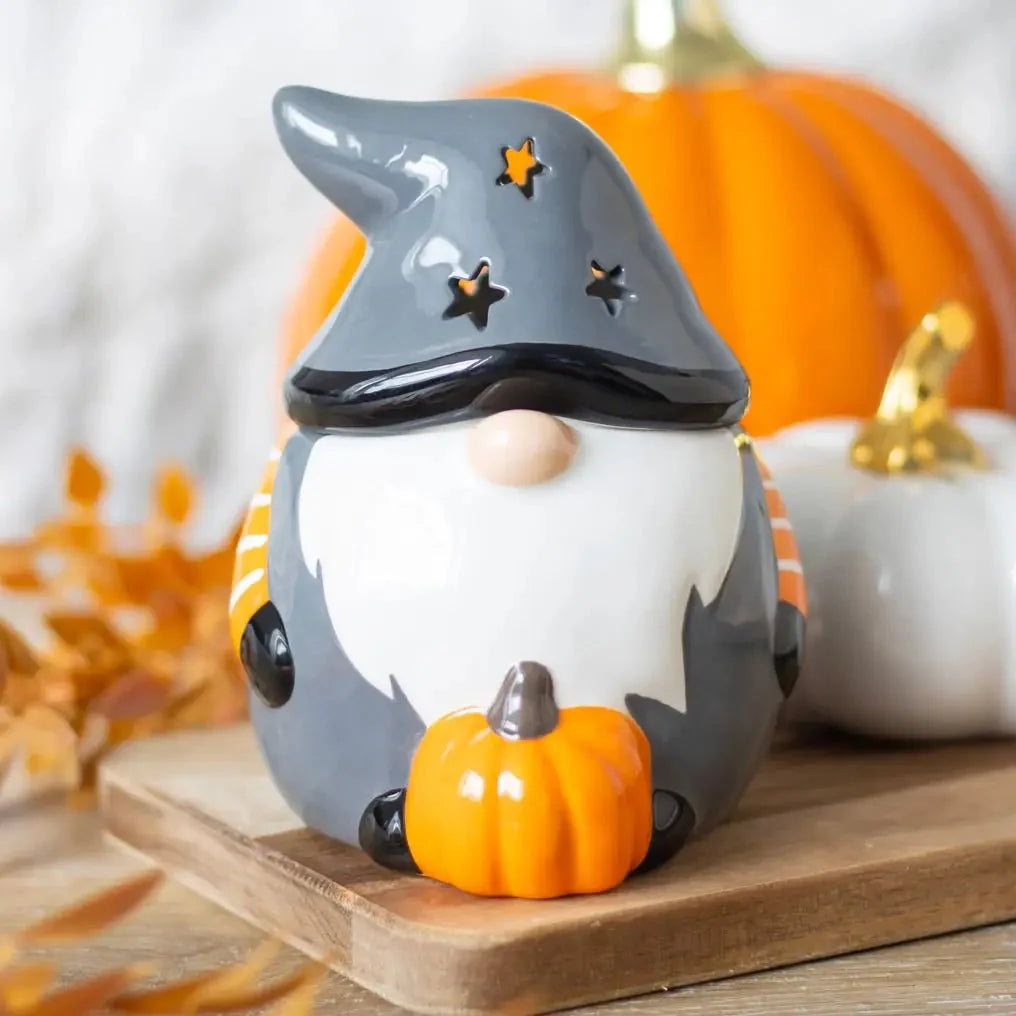 Gray gnome oil burner with star-shaped hat cutouts, white beard and an orange pumpkin, displayed on a wooden board.