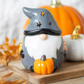 Gray gnome oil burner with star-shaped hat cutouts, white beard and an orange pumpkin, displayed on a wooden board.