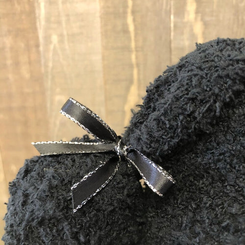 Black plush toy with a decorative bow on a wooden surface