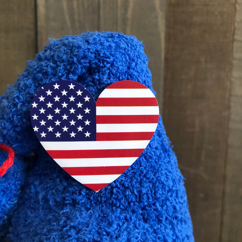 Blue teddy bear with an American flag heart emblem on a wooden background