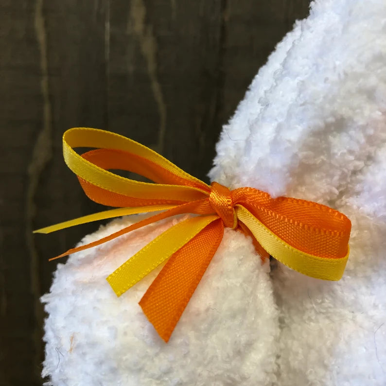 White plush toy with an orange and yellow bow on a dark background