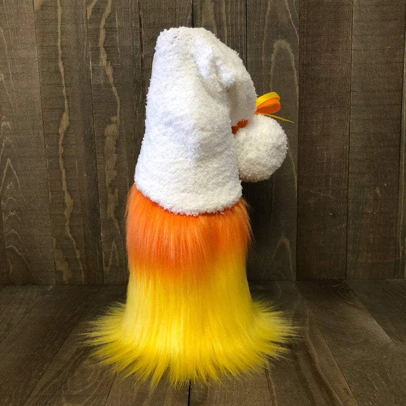 Stuffed animal resembling a candy corn with white, orange, and yellow fur against a wooden background.