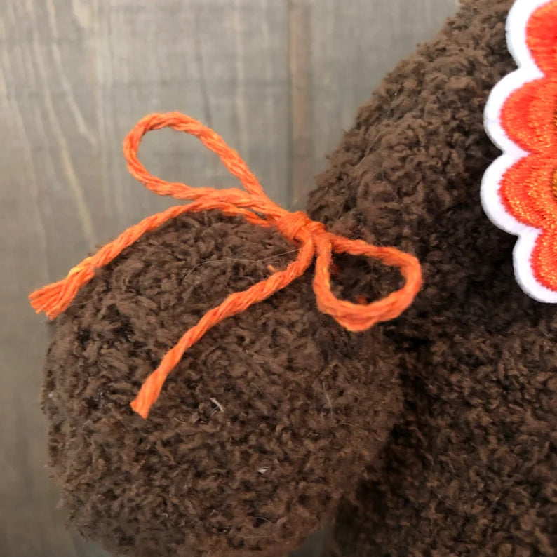 Close-up of a brown knitted item with orange yarn that is on a handcrafted Thanksgiving day gnomes arm.