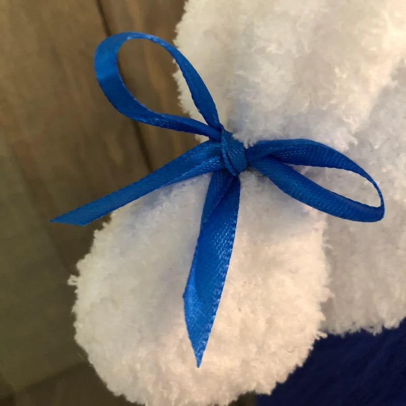 White plush toy with a blue ribbon on a wooden surface