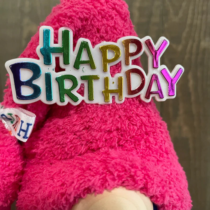 Pink plush toy with a colorful 'Happy Birthday' decoration on a wooden surface