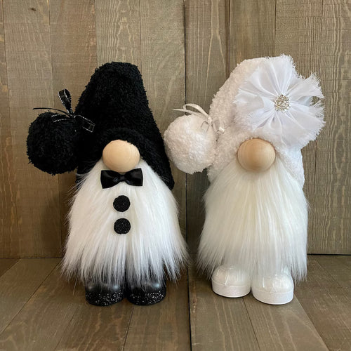 Two decorative gnomes, one black and white and one white with a large flower, on a wooden floor.