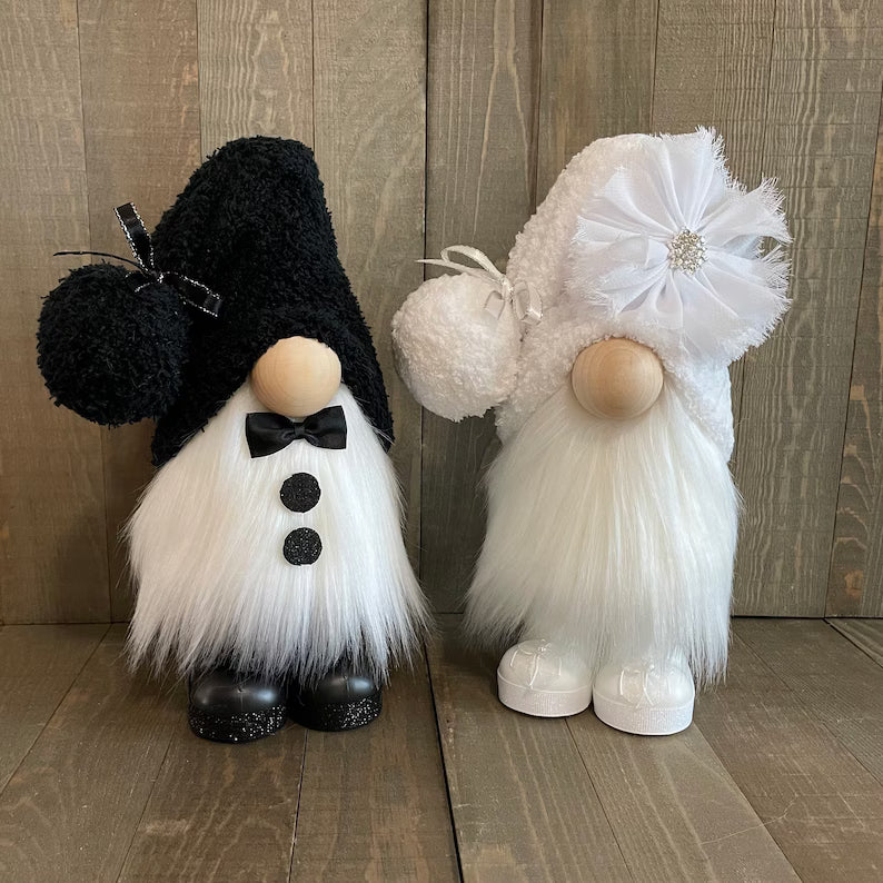 Two decorative gnomes, one black and white, the other white with a flower, on a wooden floor.