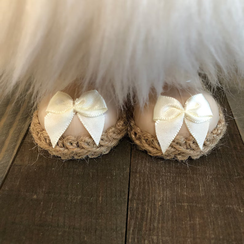 Pair of baby shoes with white bows on a wooden floor.