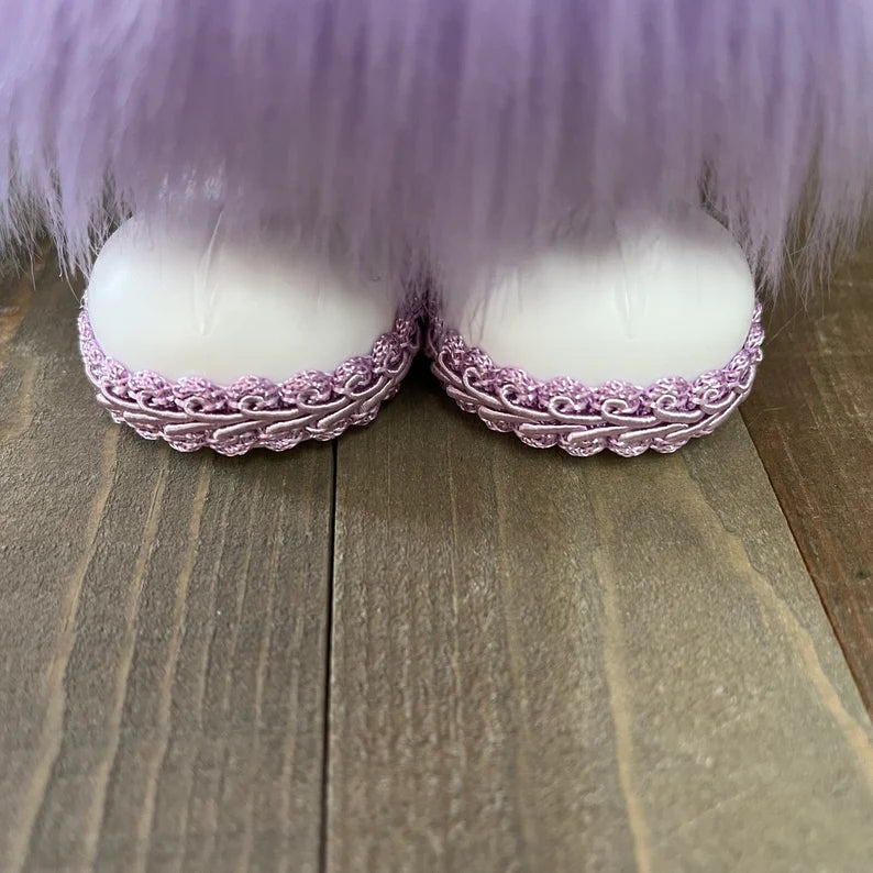 White shoes with pink lace uppers on a wooden surface, covered by purple fur.