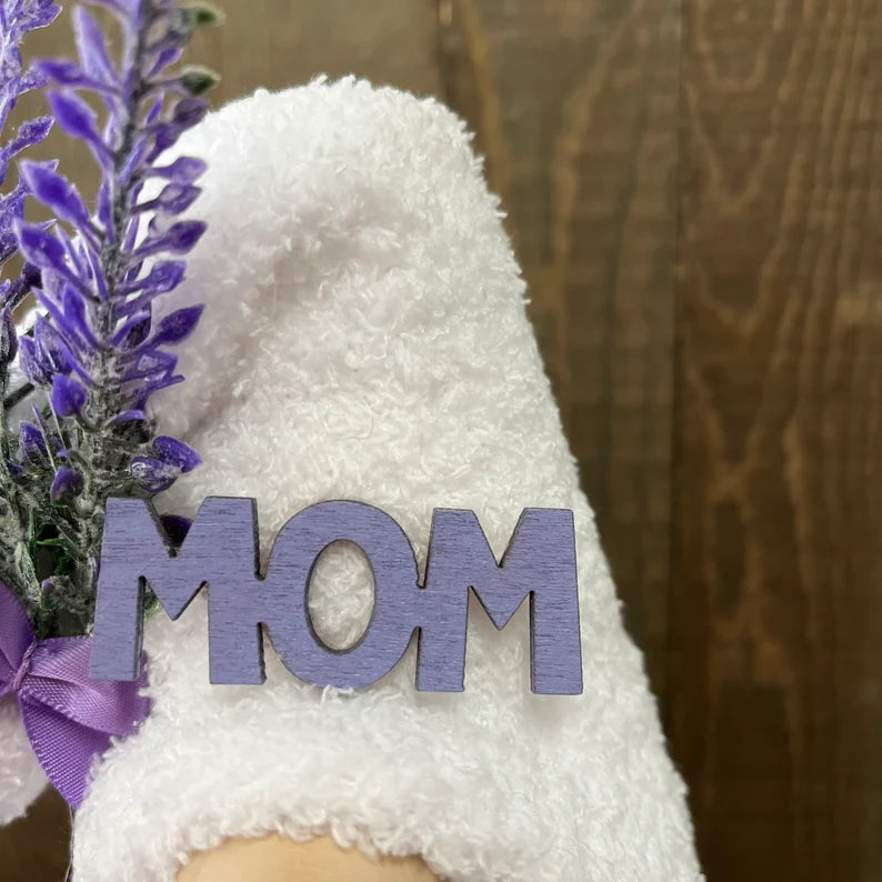 White teddy bear with a purple 'MOM' sign and lavender flowers on a wooden surface