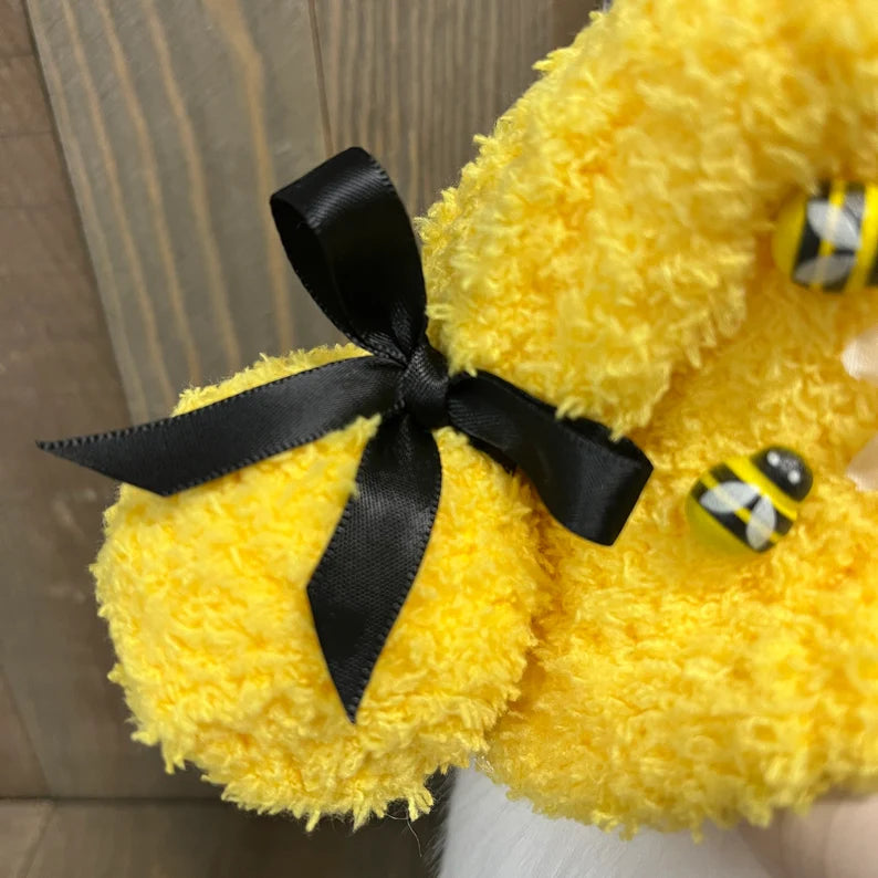 Yellow plush toy with a black bow and small bee on a neutral background