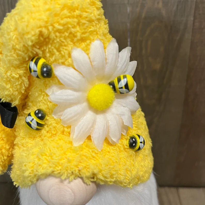 Yellow plush toy with a white flower and black and yellow bees on a wooden surface