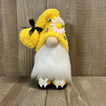 Gnome with yellow hat, white beard, and black shoes on a wooden floor.