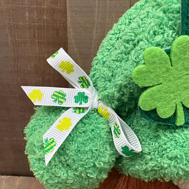 St. Patrick's day handcrafted gnome with a white ribbon featuring green clover designs on a wooden surface.